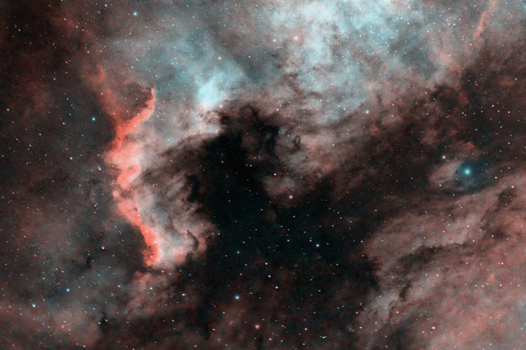 The Gulf of Mexico and the Cygnus Wall post-processed in an HOO palette: red Cygnus Wall, teal glow above the gulf, small stars